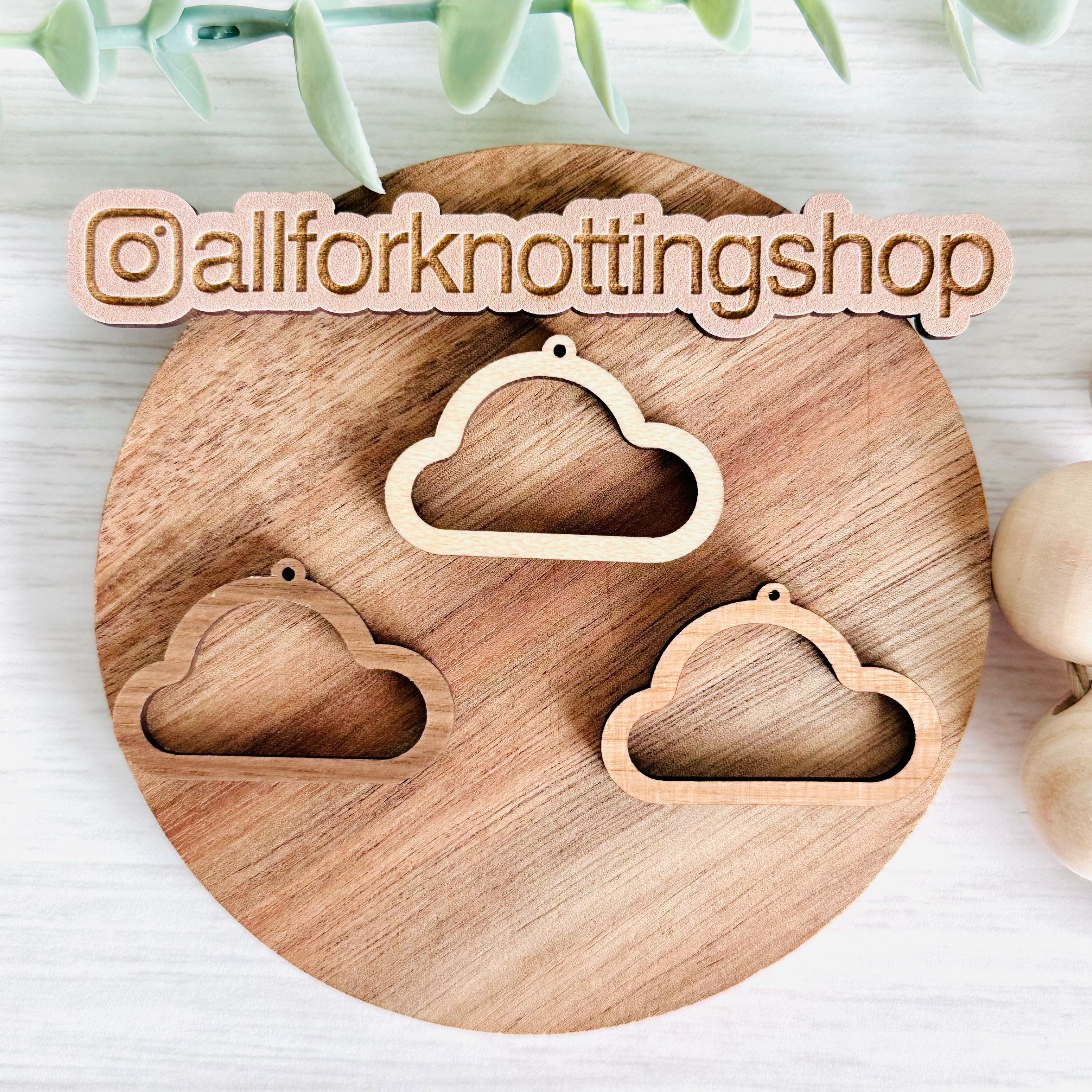 Three wooden earring blanks of different shades displayed on a wooden surface with a brand tag in the foreground.